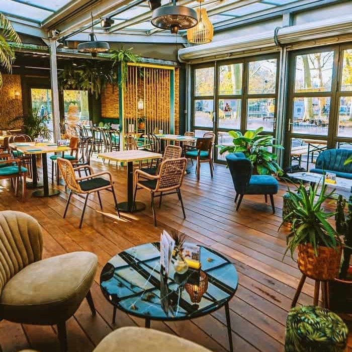 Intérieur du restaurant L’Oasis à Lille : tables, fauteuils et plantes sous la verrière.